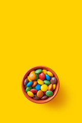 Obraz premium Colorful candies bowl on a yellow background viewed from above. Top view