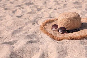 Fototapeta na wymiar Straw hat with sunglasses on sandy beach. Space for text