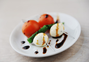 Creative serving of caprese salad. Whole tomato, mozzarella cheese ball, green basil leaf on skewers. Balsamic sauce