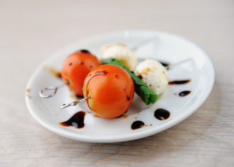 Creative serving of caprese salad. Whole tomato, mozzarella cheese ball, green basil leaf on skewers. Balsamic sauce