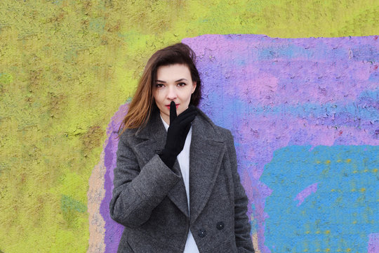 Young brunette girl covers her mouth with a finger in gloves on the background of a colorful wall.