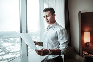 Young ceo holding some documents standing near window