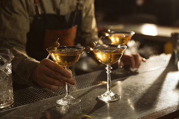 Barman with glasses of martini cocktail at counter, closeup. Space for text