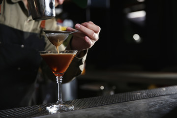 Barman pouring martini espresso cocktail into glass at counter, closeup. Space for text