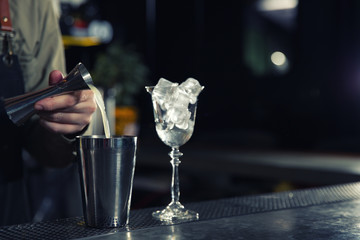 Barman pouring lemon juice for cosmopolitan martini cocktail into shaker at counter, closeup. Space for text