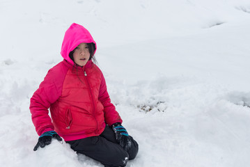 Young girl with pink hood and jacket kneeling in snow