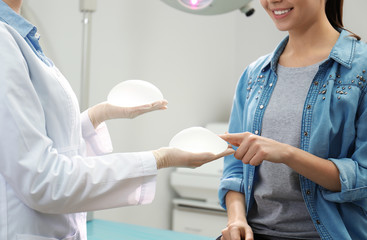 Doctor showing silicone implants for breast augmentation to patient in clinic, closeup. Cosmetic...