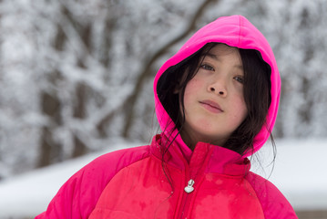 Young girl with pink hood and jacket surrounded by snow