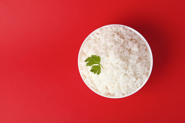 Bowl of boiled rice on color background, top view with space for text