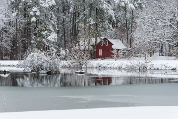 Red house in snow behind a frozen pond