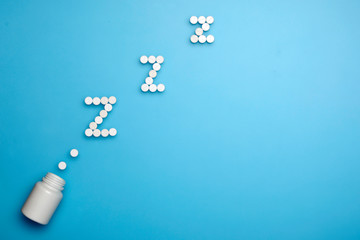 Tablets and pills. Letters ZZZ from the pills flying out of the bottle. Sleeping pills on a blue background.