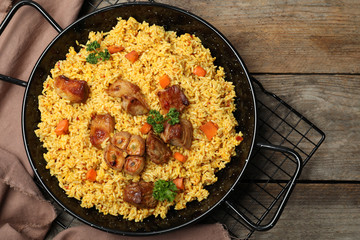 Frying pan with delicious rice pilaf on wooden background, top view
