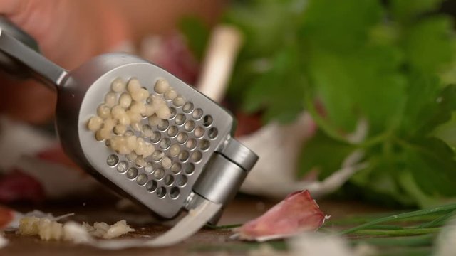 SLOW MOTION CLOSE UP DOF: Aromatic garlic juice squirts across the table as a clove is being pressed. Unrecognizable chef squeezes a raw clove of garlic with a stainless steel press. Squeezing garlic.