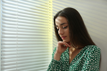 Young woman near window with Venetian blinds. Space for text