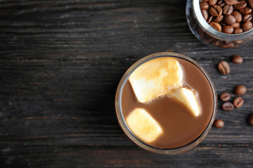 Coffee drink with milk ice cubes and beans on dark background, flat lay. Space for text