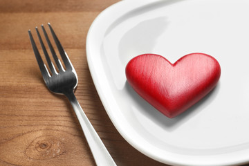 Plate with red heart and fork on wooden table, closeup. Healthy diet concept