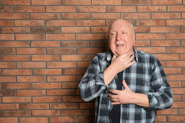 Obraz premium Senior man suffering from cough near brick wall. Space for text