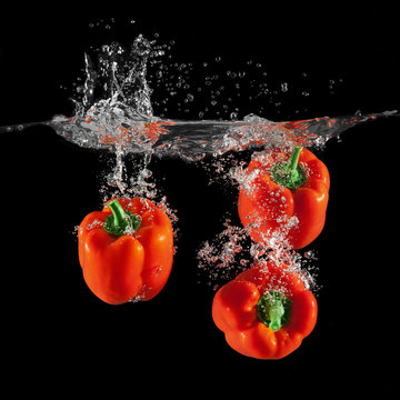 Three red bell peppers falling in water with splash on black background, paprika, stop motion photography