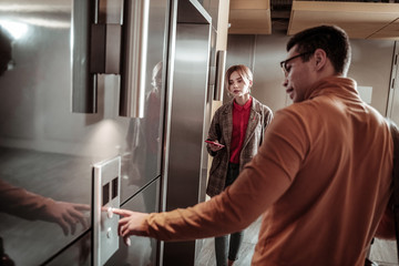 Dark-haired man wearing orange polo neck calling the elevator