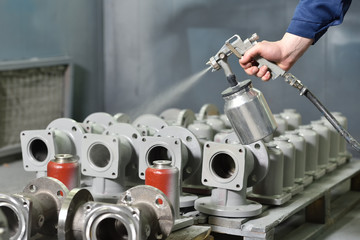 A worker at a factory in a special room paints parts of the valves from the spray gun. Paint valves...