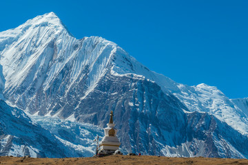 Een stoepa met Annapurna Chain als achtergrond, Annapurna Circuit Trek, Himalaya, Nepal. Hoge bergen bedekt met sneeuw. Het land voor de stoepa is kaal en droog. Een gebedsvlag ernaast.
