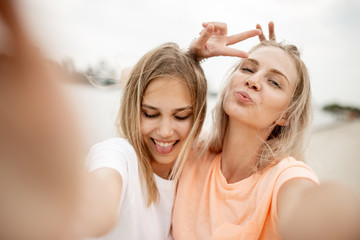Two young attractive blonde girls take a selfie on the beach on a warm windy day
