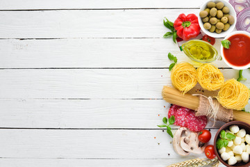 Ingredients for cooking pasta. Dry pasta. Mushrooms, sausages, tomatoes, vegetables. Top view. On a white wooden background. Free copy space.