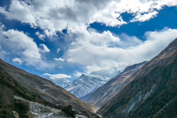 Fototapeta premium Himalayas, Annapurna Circuit Trek, Himalayas, Nepal. Endless mountain chains in the back, covered with clouds and snow. Dry, steep slopes. Freedom, wilderness. Bright sunlight comes through clouds