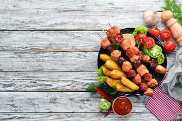 Chicken shish kebab with potatoes and vegetables on a white wooden background. Meat. Top view. Free...