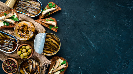 Assortment of sprats in oil. Smoked fish On a black background. top view. Free copy space.