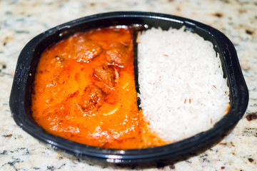 Orange red curry tikka masala sauce macro closeup, with white basmati rice in black plastic tv dinner fast food frozen quick meal container on table