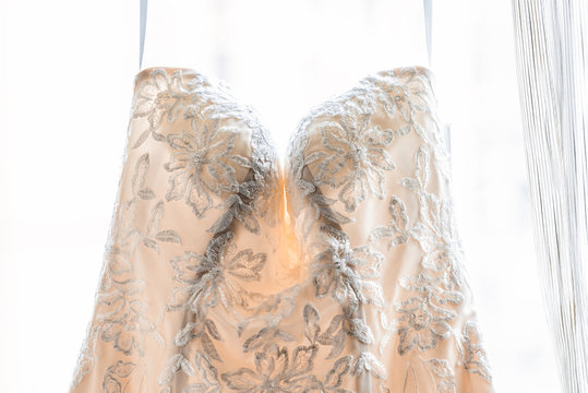 Closeup of wedding dress hanging in front of window, with bilds, isolated white background showing detail and texture of romantic lace material flowers floral pattern