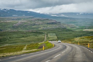 Ring road in east Iceland highlands highway with barren bare green landscape and car on steep slope with route 1 in overcast cloudy stormy weather near Egilsstadir