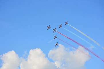 Fototapeta na wymiar Formation of six stunt jets flying on a cloudy blue sky leaving red and white smoke trails