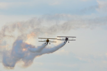 Fototapeta na wymiar Two stunt biplanes flying side by side on a cloudy blue sky leaving white smoke trail