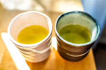 Wooden table in house room with morning sunlight and two cups filled with Japanese vibrant green yellow oolong tea color in breakfast container