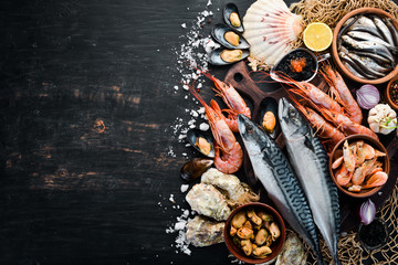 Seafood. Fresh fish, shrimp, oysters and caviar on a black wooden background. Top view. Free copy space.