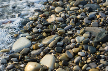 pebble stones on the sea beach, the rolling waves of the sea with foam