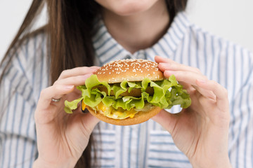 Slender brunette girl holds in her hands a hamburger. On a white background, the theme of diet and proper nutrition,