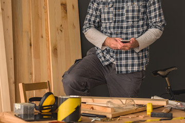Carpenter using smartphone in small business woodwork workshop