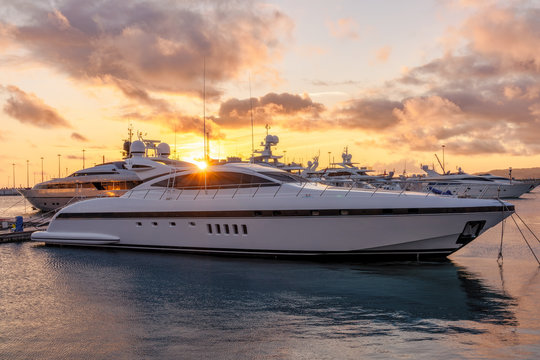 Beautiful orange sunset in the sea harbor with moored yachts. Expensive 92 foot yacht at the pier during sunset