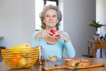 Pensive retired lady enjoying coffee break at home