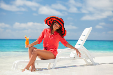 Obraz na płótnie Canvas Fashion woman drinking cocktail on the beach. Happy island lifestyle. White sand, blue cloudy sky and crystal sea of tropical beach. Vacation at Paradise. Ocean beach relax, travel to Maldives islands