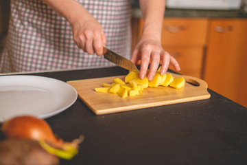 housekeeper cuts potatoes for soup and puts it on the plate