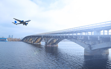 The plane over the river and the long bridge in the city the sun shines.