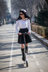 Woman riding a scooter. Brunette pushes off the road.