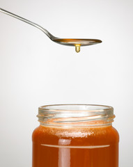 SPOON FULL OF HONEY DRIPPING INTO GLASS JAR OF HONEY