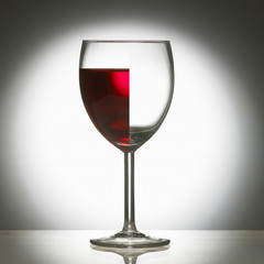 WINE GLASS WITH LEFT SIDE FULL OF RED WINE AND RIGHT SIDE EMPTY