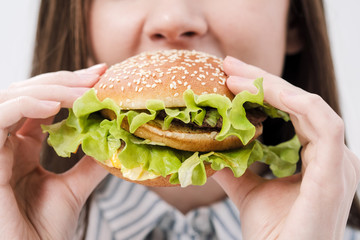 Young beautiful brunette girl on a white background with a hamburger in her hands. Eating with pleasure fast food.