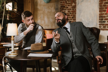 Two bearded men wearing old fashioned suits talking or discuss something in the restaurant